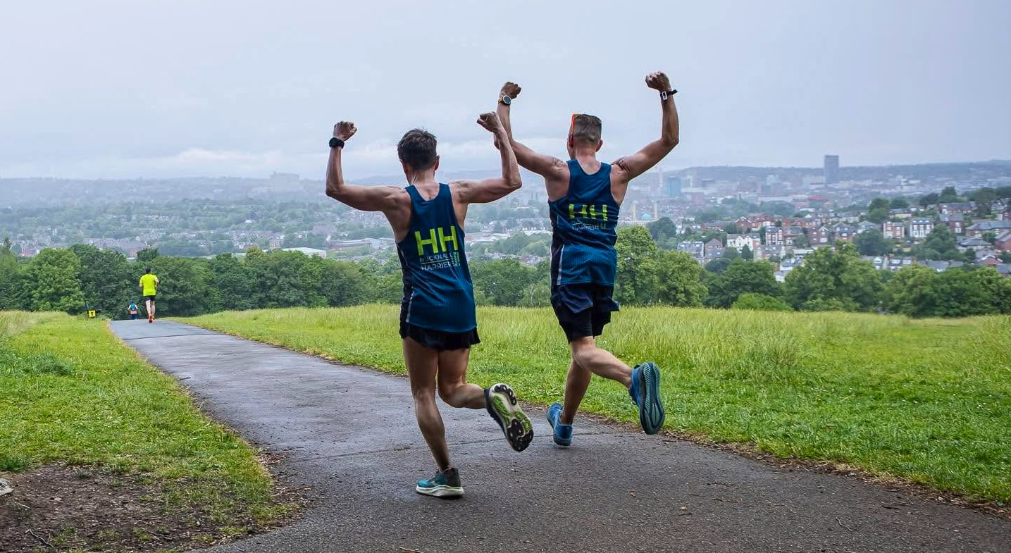 Two runners celebrating together on a hillside path overlooking Sheffield